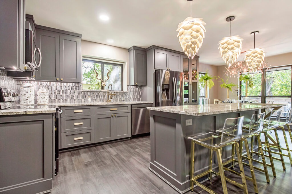 Modern kitchen with gray cabinets, granite countertops, and unique pendant lights. A large window offers natural light, enhancing the space's inviting atmosphere.