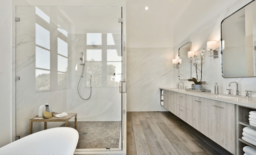 Modern bathroom with a glass shower, double vanity, and large windows providing natural light. Features elegant fixtures and a sleek design.