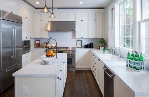 Bright, modern kitchen featuring white cabinetry, quartz countertops, and stainless steel appliances. A fruit centerpiece adds warmth to the space.