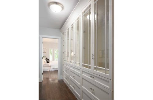 Spacious hallway featuring stylish white cabinetry with glass doors and drawers, leading to a bright room in the background.